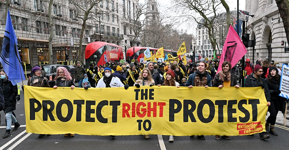 Eight protestors hold a long yellow Extinction Rebellion banner which reads 'Protect The Right To Protest' as they lead a protest march along a central London street.