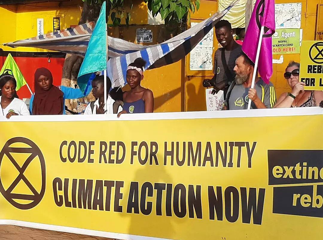 Rebels stand behind a long yellow Extinction Rebellion banner which reads 'Code Red For Humanity - Climate Action Now.'