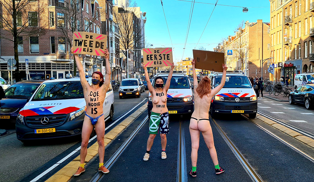 People stand in the middle of the road, holding signs and with text painted onto their bodies